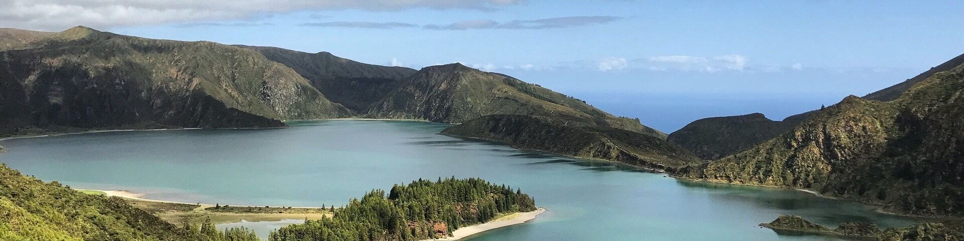 Paisagem montanhosa com um lago grande, rodeado por florestas densas e colinas.