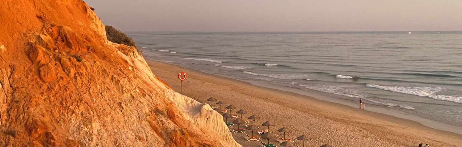 A beach with a wooden boardwalk, umbrellas, and a cliff.