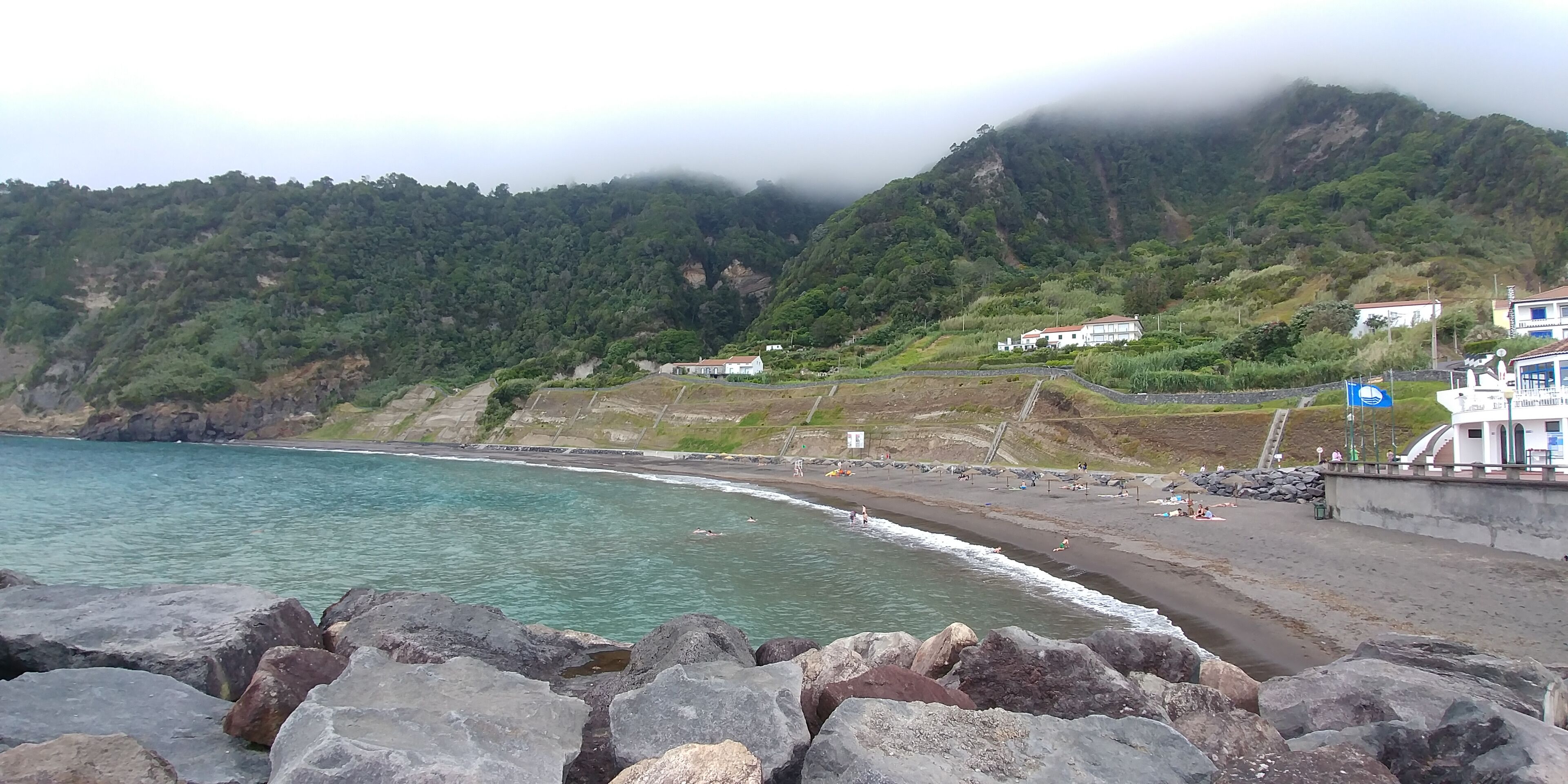 A coastal landscape with a rocky shoreline, a beach, and buildings on a hillside.