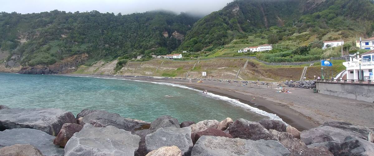 A coastal landscape with a rocky shoreline, a beach, and buildings on a hillside.