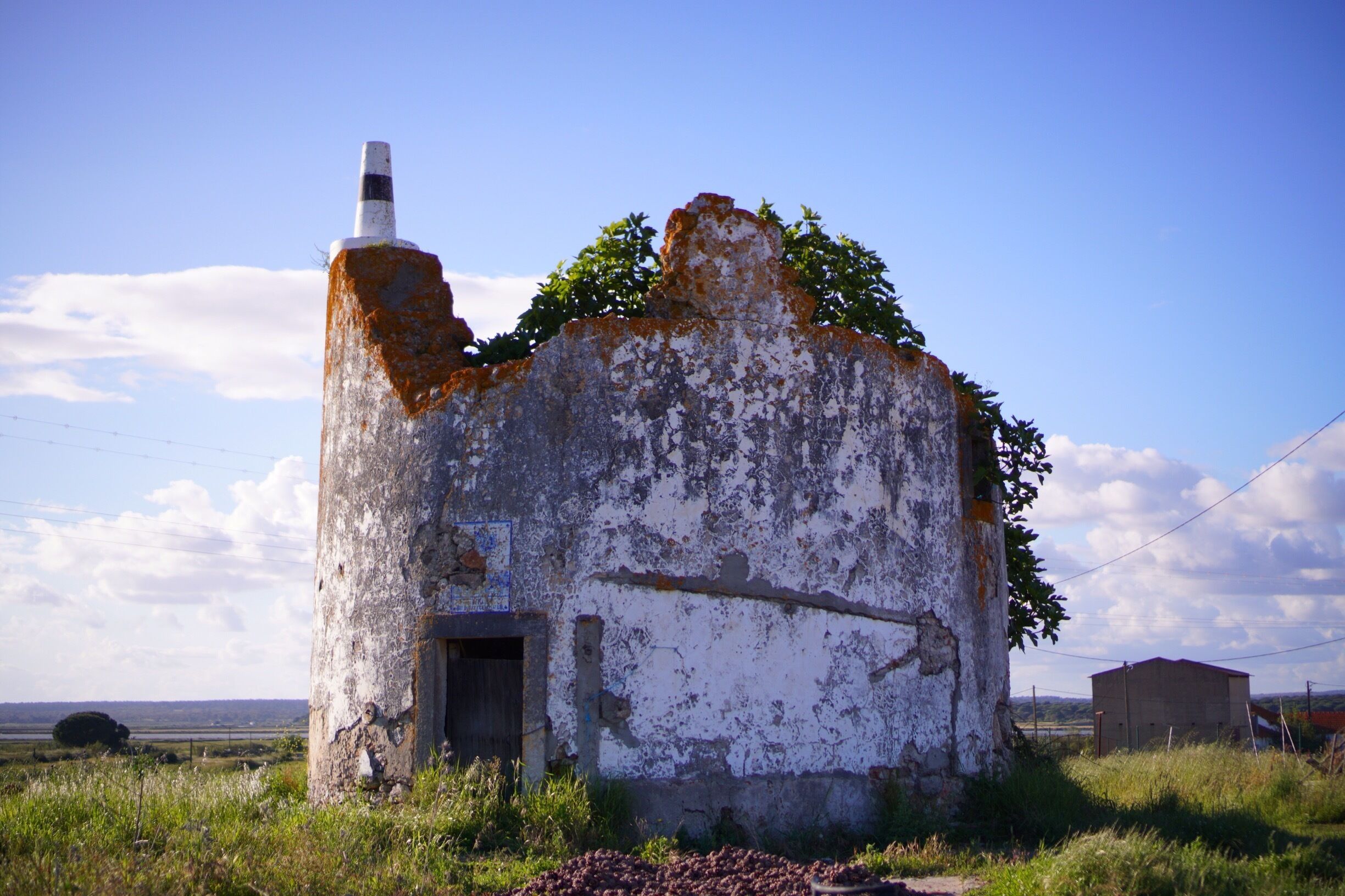 An old, weathered building with a chimney, surrounded by grass and a clear sky.