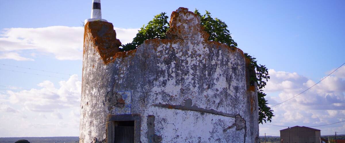An old, weathered building with a chimney, surrounded by grass and a clear sky.