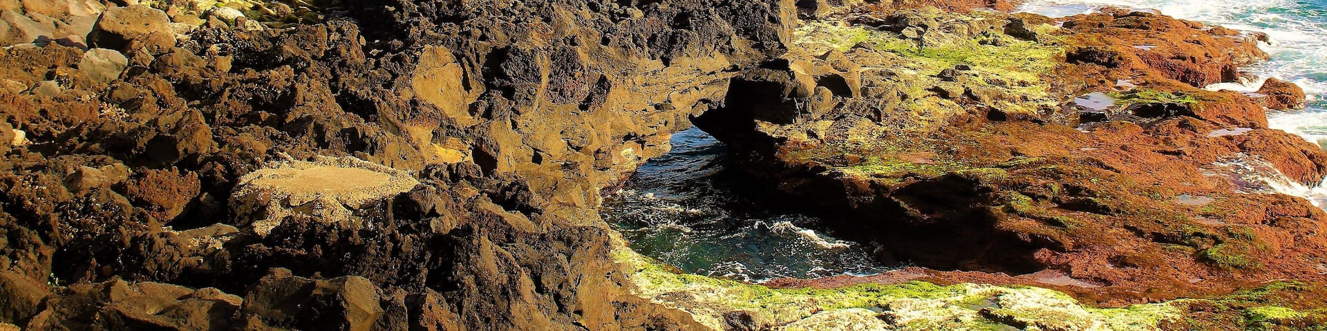 A rocky coastline with a person in a red jacket standing on a cliff overlooking the ocean.