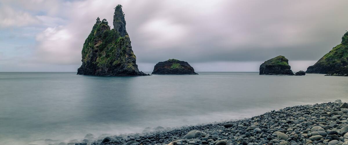 A rocky shoreline with large boulders and a prominent tree-covered rock formation in the distance.