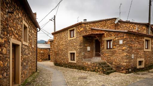 Una estrecha calle adoquinada bordeada por edificios de piedra con arquitectura tradicional, que incluyen una escalera de madera que lleva a una puerta.