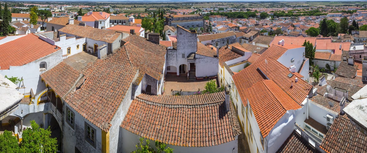 A historic town with terracotta-tiled rooftops, white buildings, and a clear blue sky.