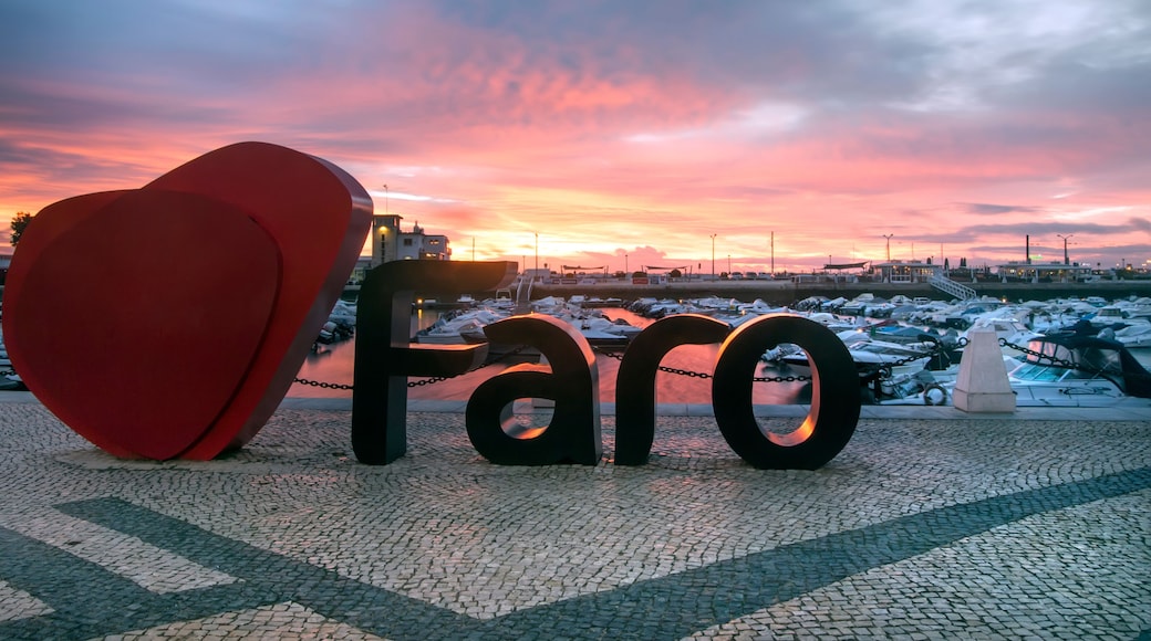 A sunset with the word 'Faro' in large letters, a red heart sculpture, and a marina with boats.