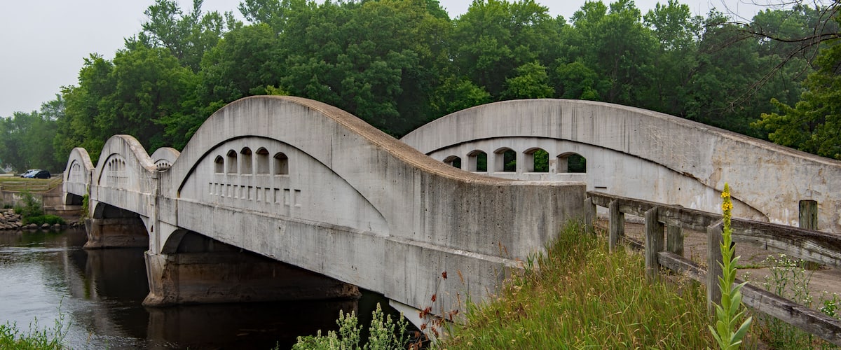 A concrete bridge over a river with greenery in the background.