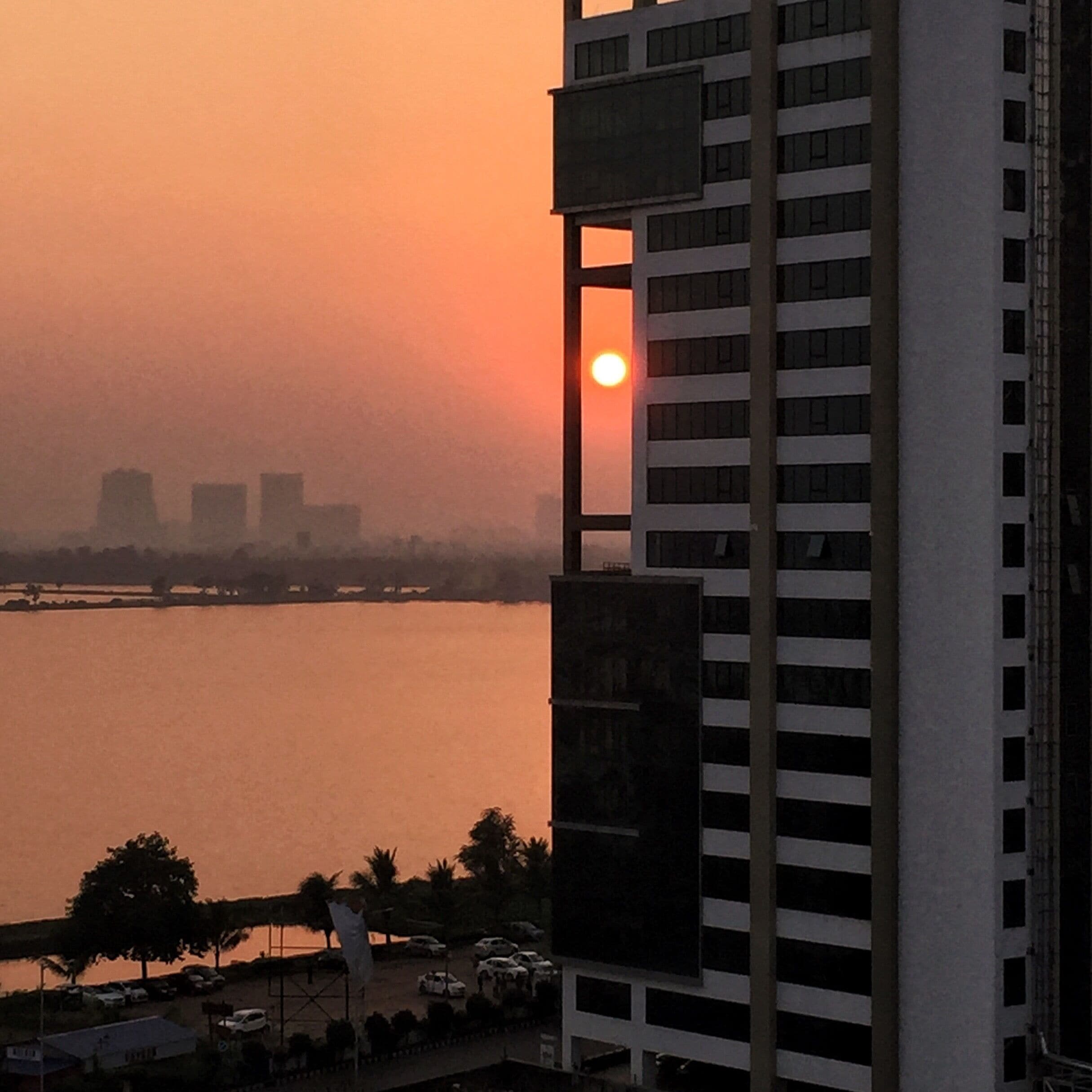 Pôr do sol sobre um corpo d'água, com edifícios ao primeiro plano.