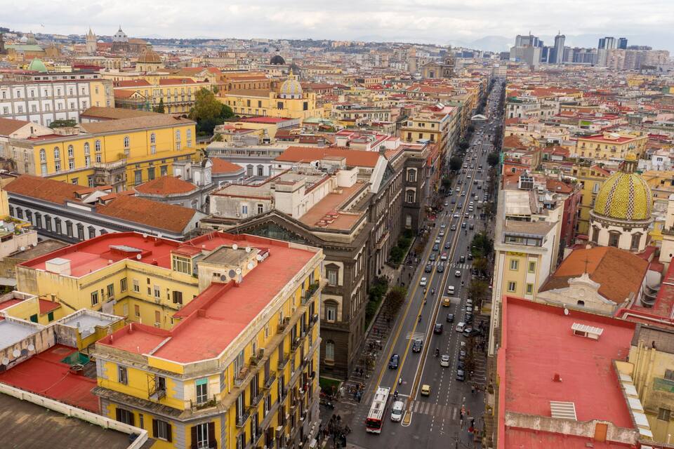 Paisagem urbana com um edifício amarelo em destaque, teto vermelho, rua movimentada e uma grande cúpula amarela.