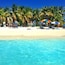 Ein Strand mit klarem türkisblauem Wasser, Palmen und Menschen, die unter bunten Sonnenschirmen entspannen.