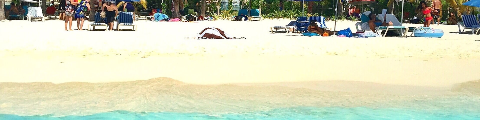 A beach with clear turquoise water, palm trees, and people relaxing under colorful umbrellas.