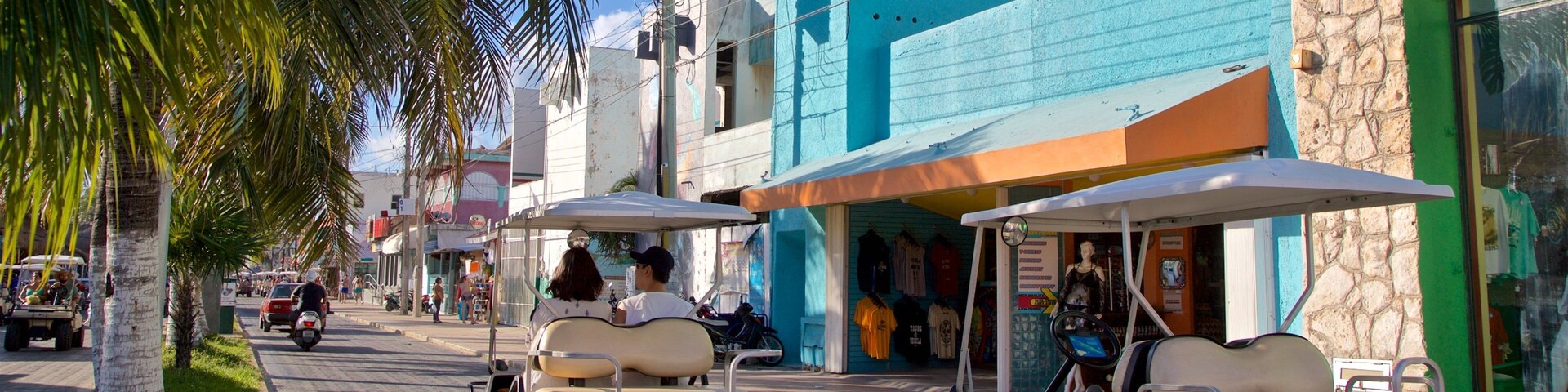 Una calle con palmeras, un edificio azul y un carrito de golf.