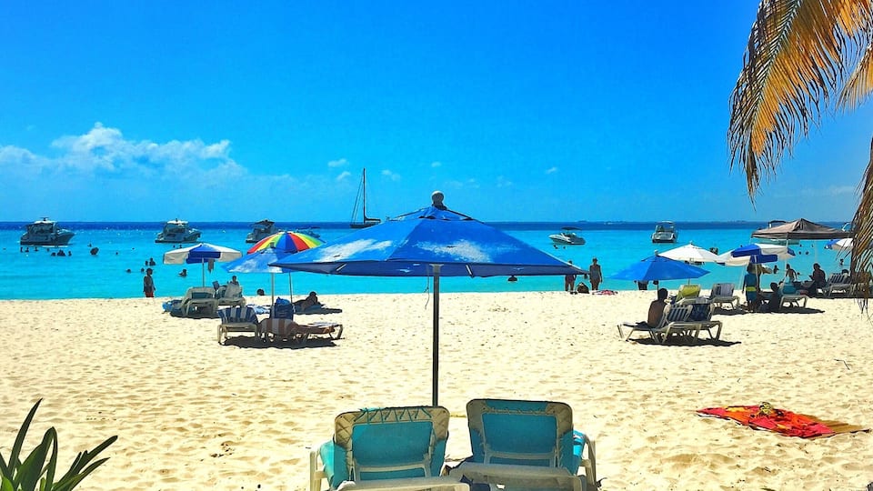 A beach with clear blue water, several boats, and umbrellas.