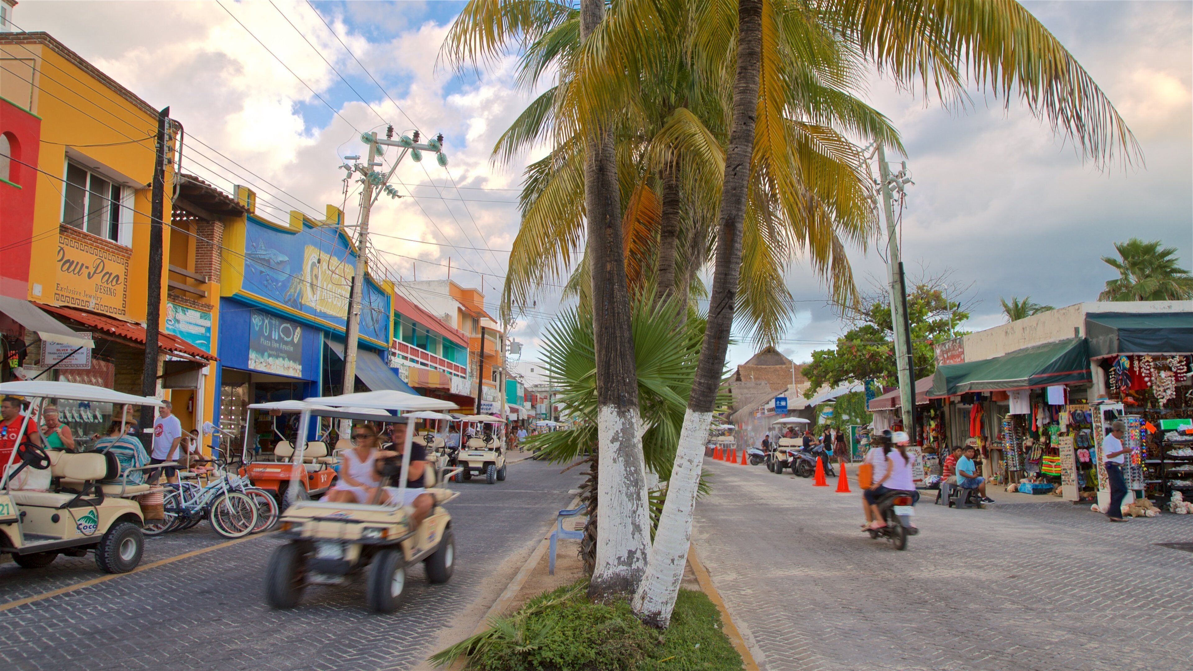 Una calle animada con edificios coloridos, una palmera y una zona de mercado.