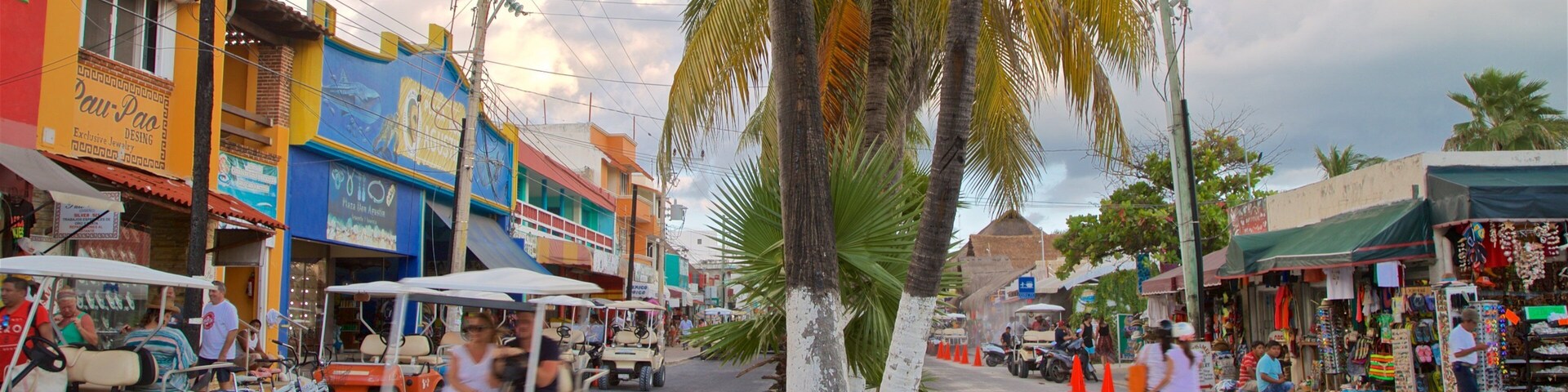 Una calle animada con edificios coloridos, una palmera y una zona de mercado.