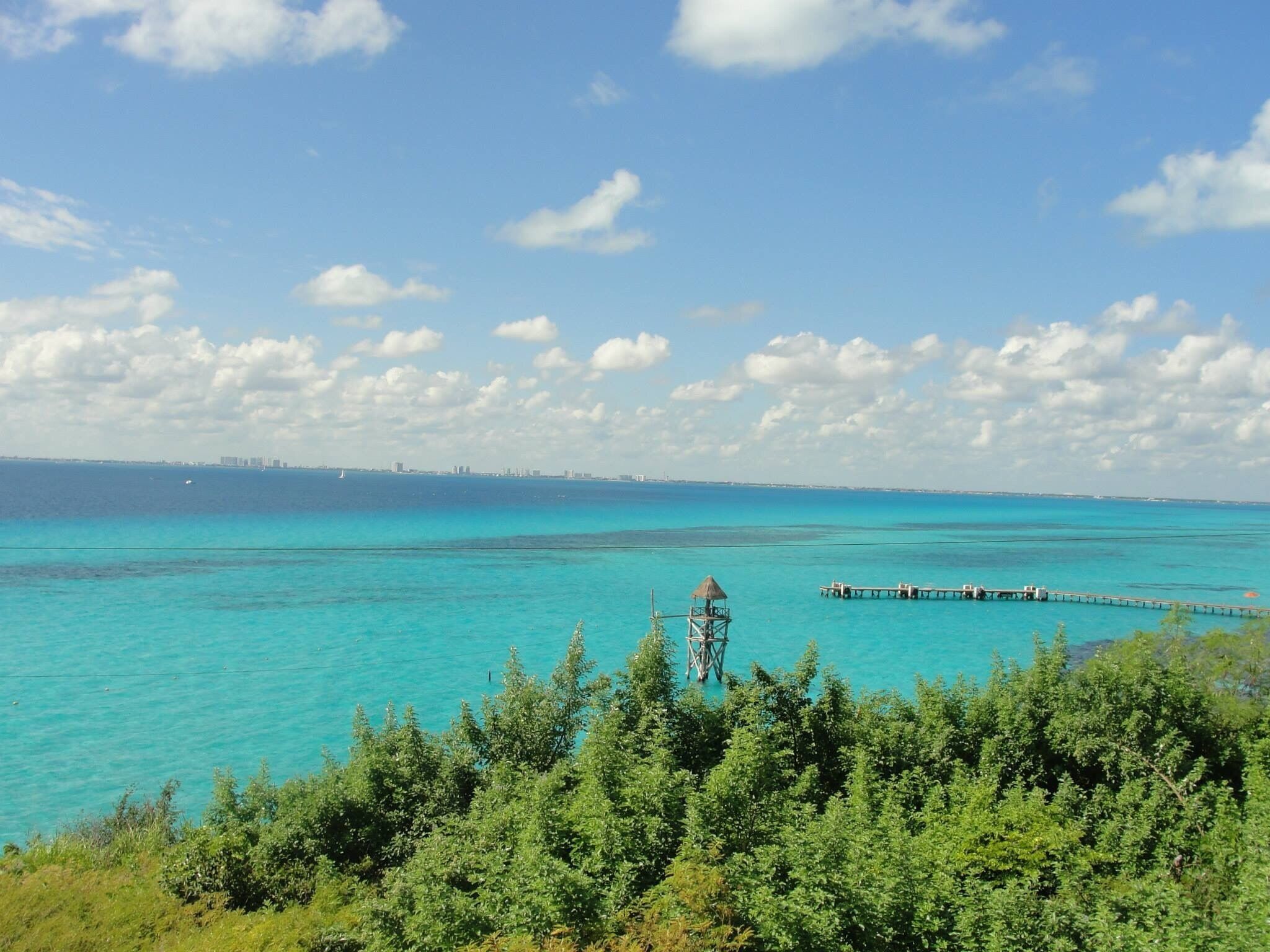 Un paisaje costero con aguas turquesas, un muelle y una estructura de techo de paja.