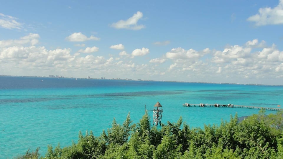 Un paisaje costero con aguas turquesas, un muelle y una estructura de techo de paja.