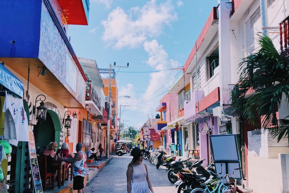 A narrow street lined with colorful buildings, parked motorcycles, and a woman walking down the road.