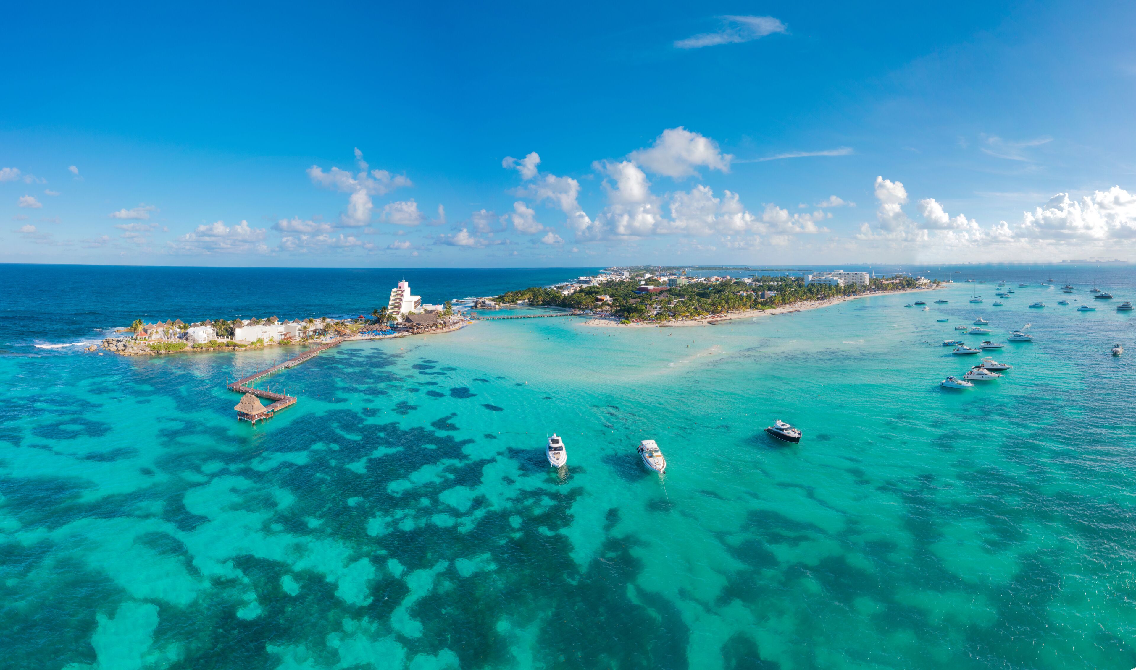 A tropical island with clear turquoise waters, a pier, and several boats.