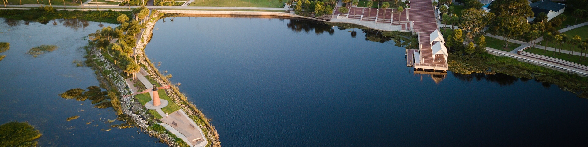 Vista aérea de un lago con un muelle, rodeado de edificios y vegetación.