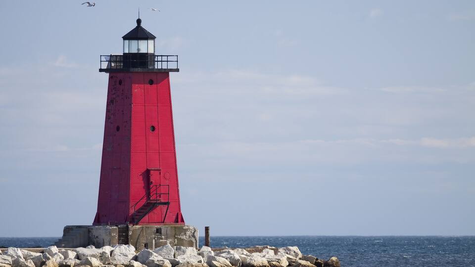 A red lighthouse on a rocky outcrop by the sea.