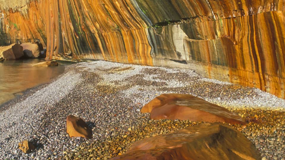 A rock formation with striations and a pebbled beach.