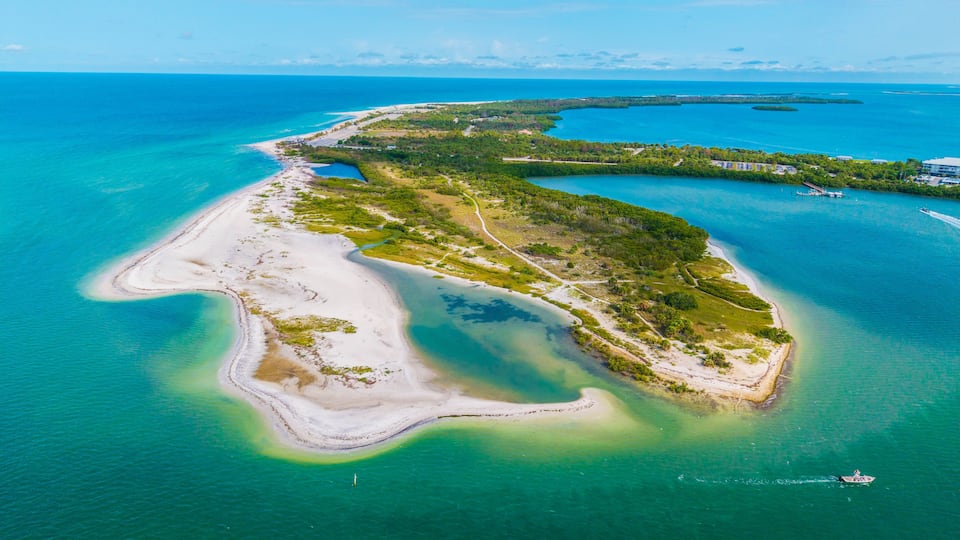 An aerial view of a coastal island with clear turquoise waters, sandy beaches, and lush greenery.