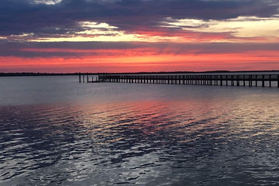 Ein Sonnenuntergang über ruhigem Gewässer mit einem sich ins Wasser erstreckenden Steg.