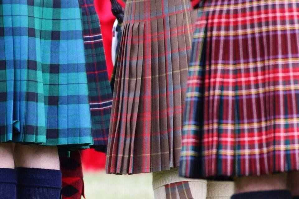 Un gruppo di persone che indossano tradizionali kilt scozzesi, con motivi e colori diversi.