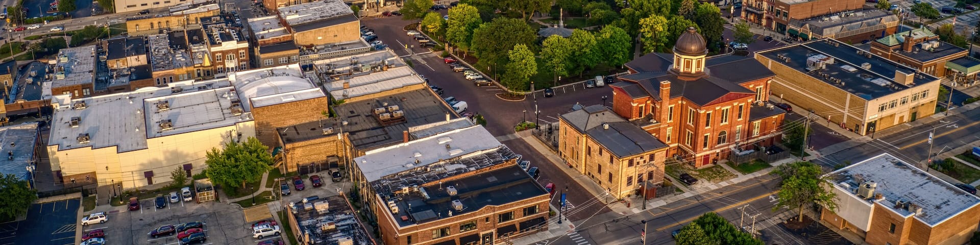 An aerial view of a town with a mix of historic and modern buildings, a central church, and surrounding green spaces.