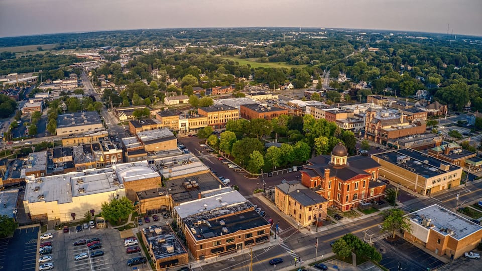 An aerial view of a town with a mix of historic and modern buildings, a central church, and surrounding green spaces.