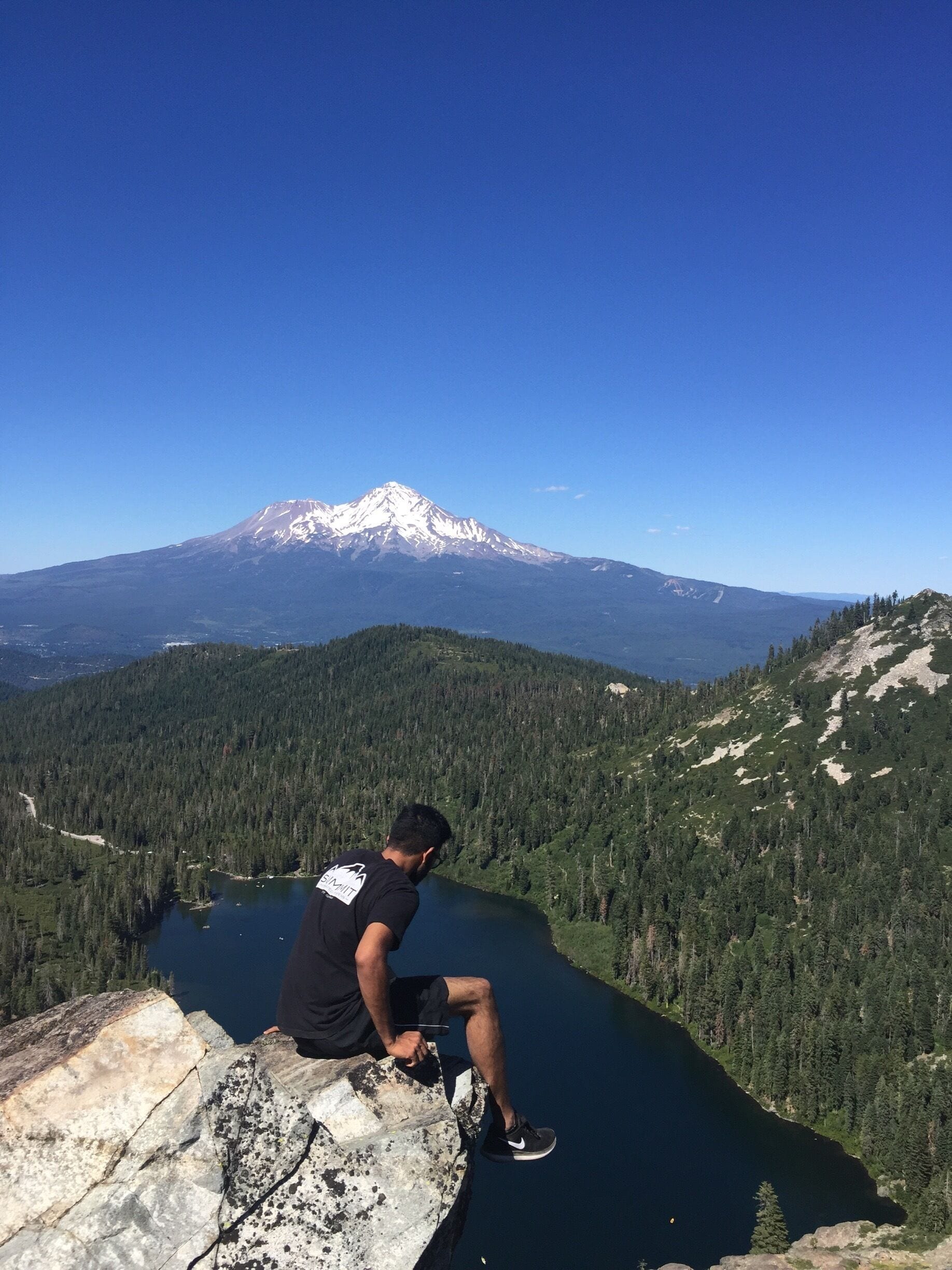 A person sitting on a rock overlooking a lake with a mountain in the background.