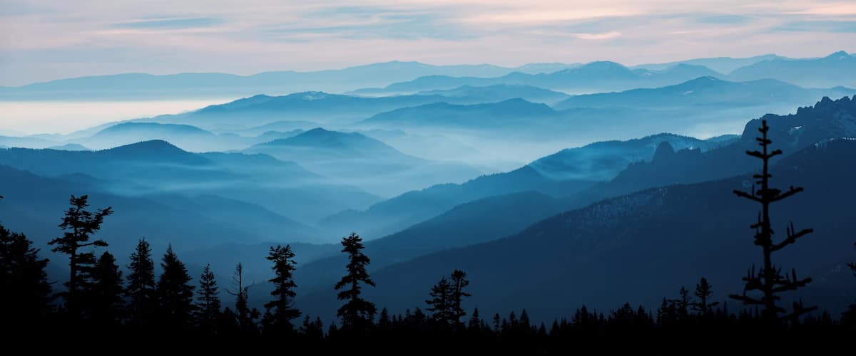 A mountain range with a forested foreground and a misty atmosphere.