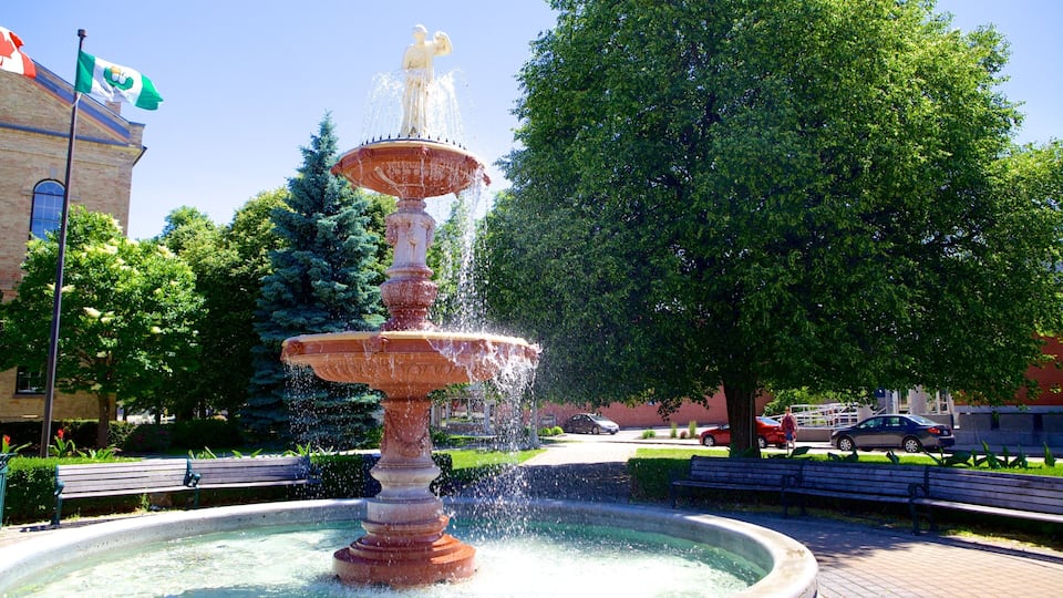 A multi-tiered fountain with water jets, surrounded by trees and benches in a park.