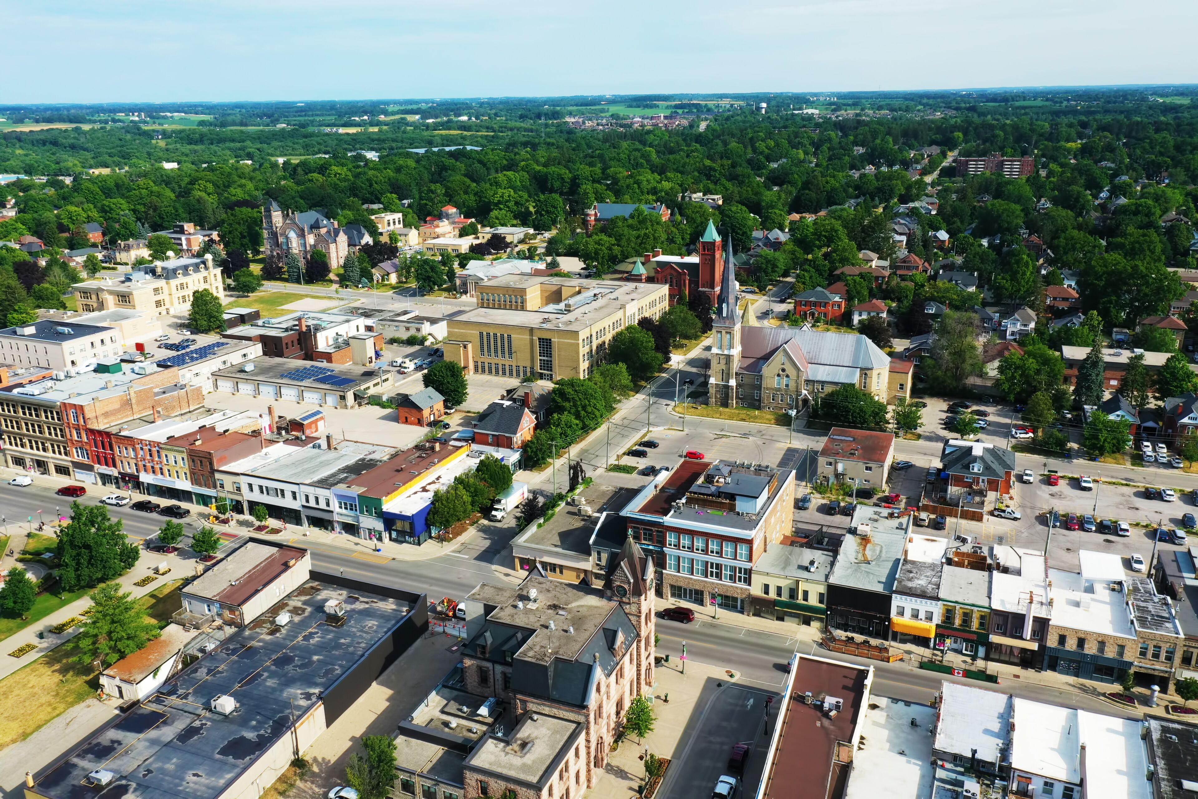 An aerial view of a town with a prominent church steeple, a mix of commercial and residential buildings, and a green landscape in the background.