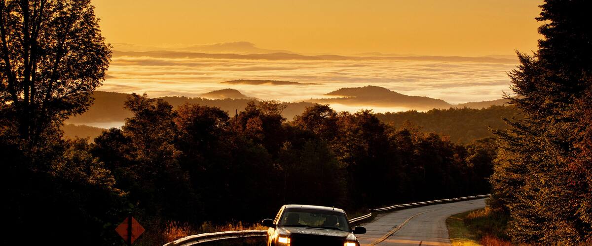 A car driving on a winding road surrounded by trees and hills during sunset.