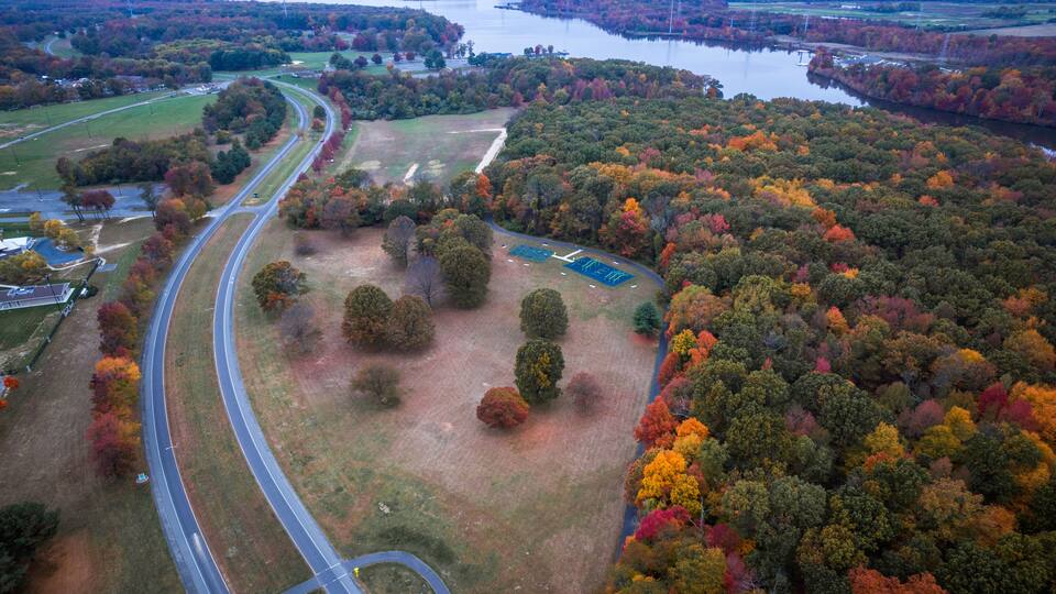 An aerial view of a winding road through a forested area with a river in the background.