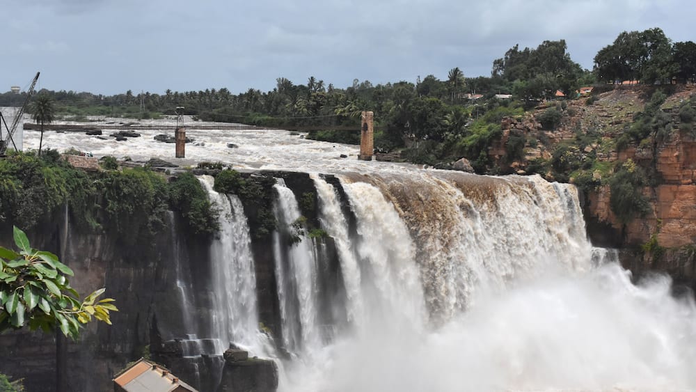 Une grande cascade comportant plusieurs chutes d’eau, une structure en briques et une forêt dense en arrière-plan.