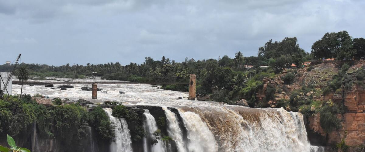 A large waterfall with multiple cascades, a brick structure, and a dense forest in the background.