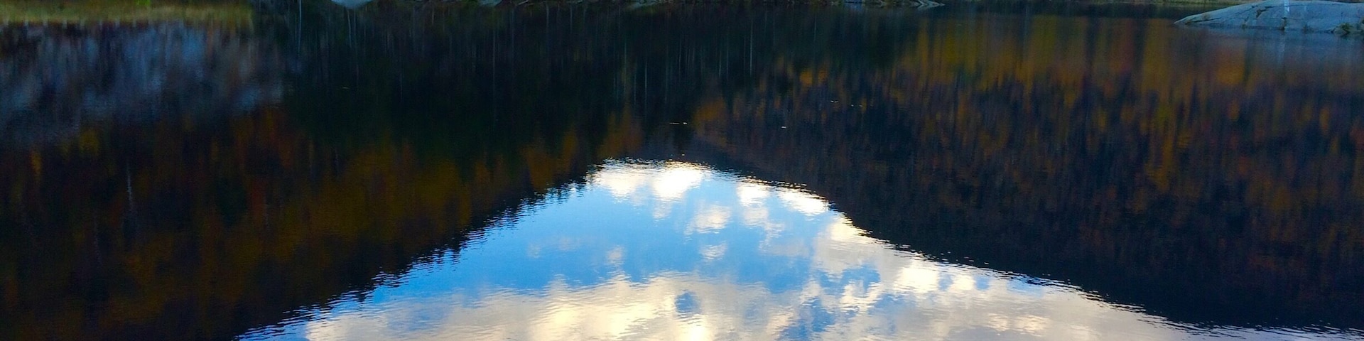 A calm lake surrounded by autumn-colored trees and rocky shores.