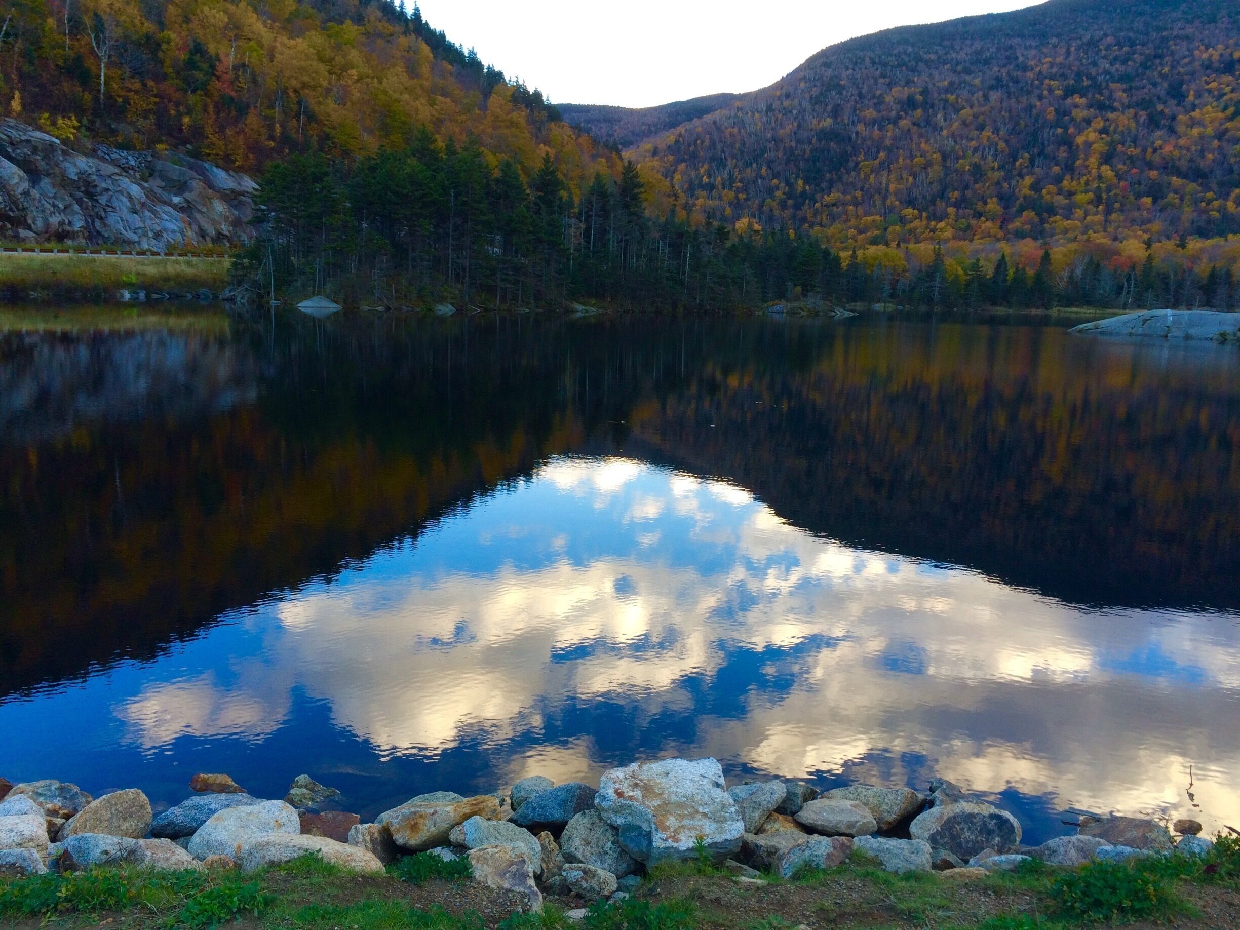 A calm lake surrounded by autumn-colored trees and rocky shores.