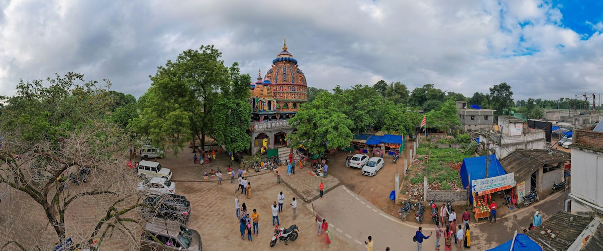 A colorful temple with a large dome, surrounded by trees and a busy street with people and vehicles.