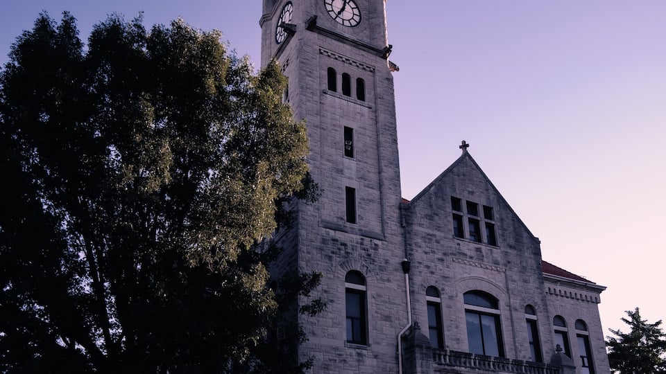 A large stone building with a clock tower, arched windows, and a red roof.