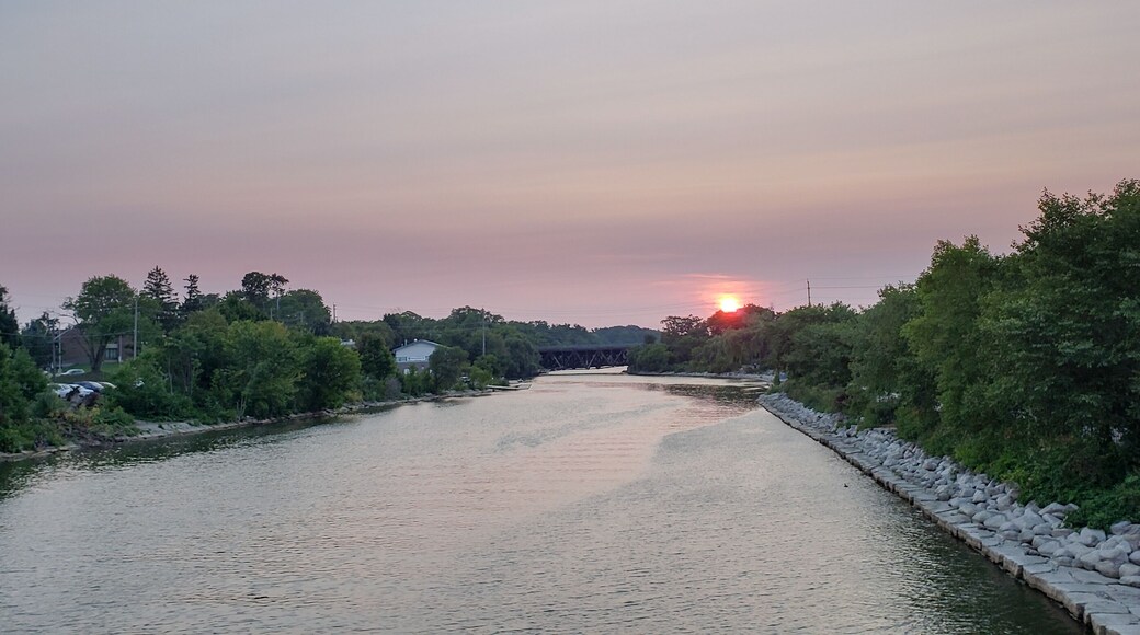 A river with a stone wall on one side and trees on the other, under a sunset sky.