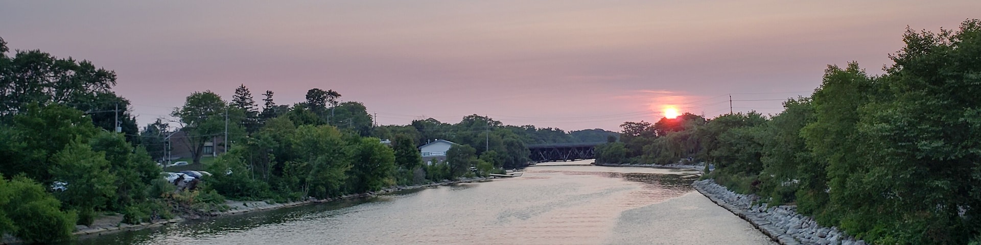 A river with a stone wall on one side and trees on the other, under a sunset sky.