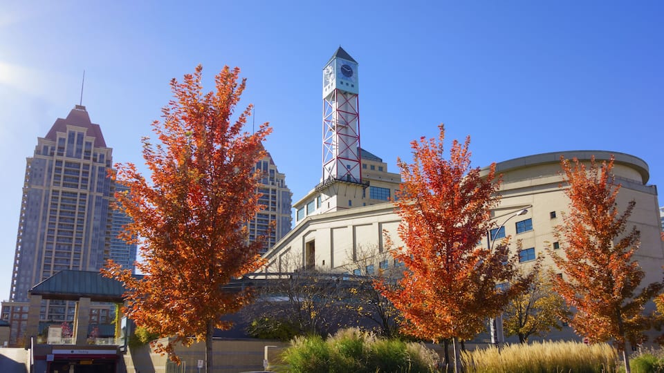 A cityscape with a prominent clock tower, autumn foliage, and modern buildings.