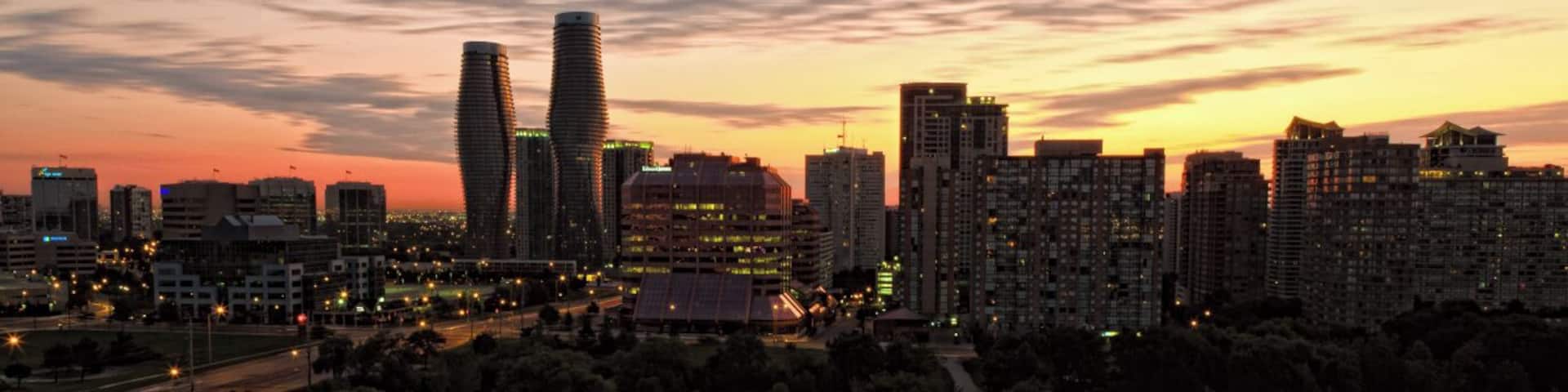 A city skyline at dusk with illuminated buildings and a sunset sky.