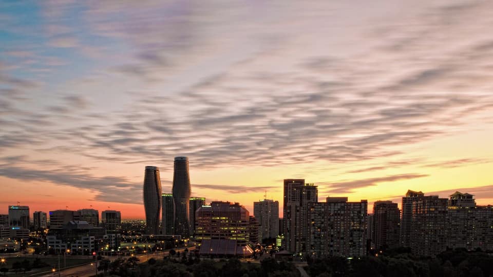 A city skyline at dusk with illuminated buildings and a sunset sky.