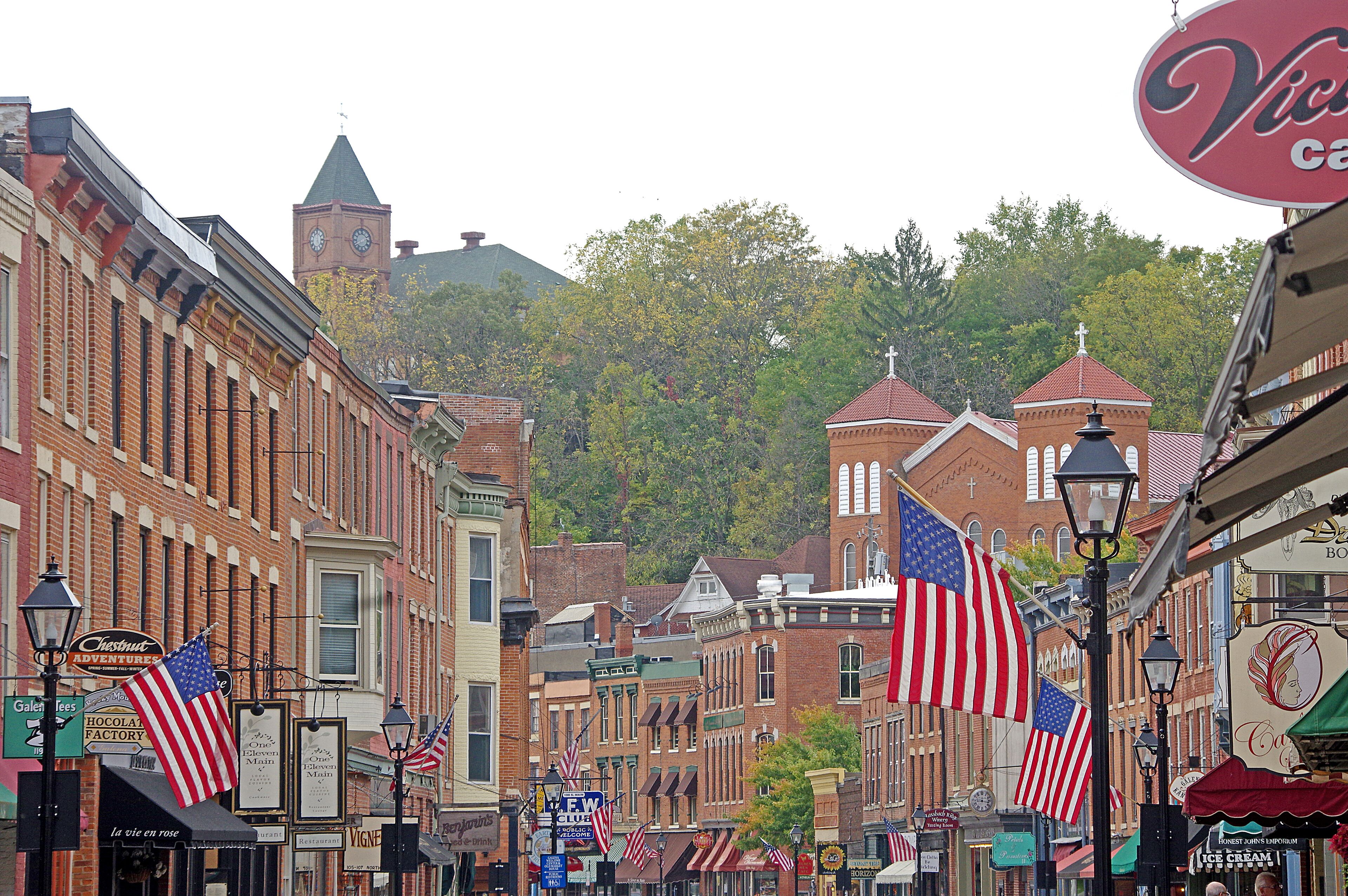 A historic downtown street with American flags, vintage buildings, and a clock tower.